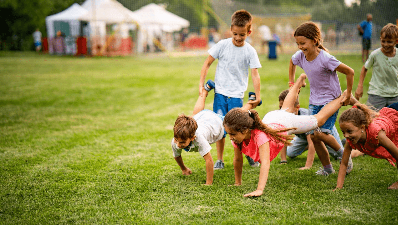 A group of children doing a wheelbarrow race in a grassy field.