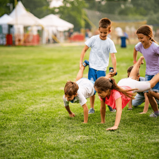 A group of children doing a wheelbarrow race in a grassy field.
