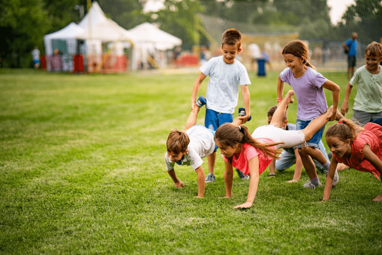 A group of children doing a wheelbarrow race in a grassy field.